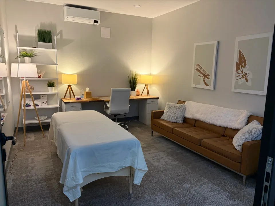 The treatment room at The Pelvic Sanctuary, with a therapy table, warm lamps and a leather sofa